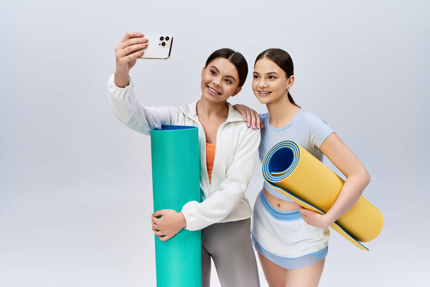 Zwei hübsche, brünette Teenager-Mädchen in sportlicher Kleidung stehen nebeneinander in einem Studio. - Foto, Bild