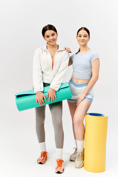 İki güzel esmer genç kız spor giysileri içinde beyaz bir arka planın önünde güvenle yan yana duruyorlar.. - Fotoğraf, Görsel