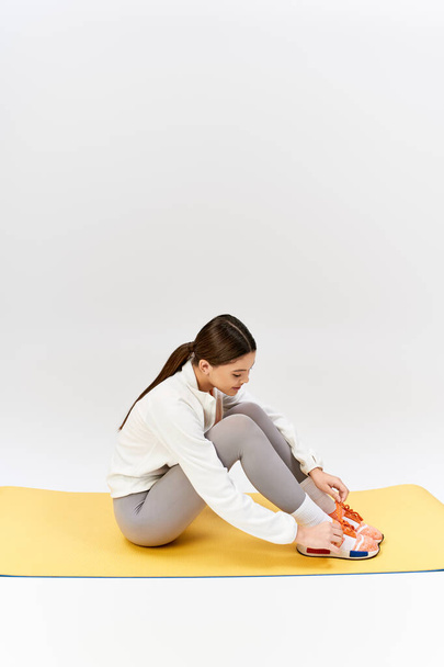 Hezká, brunetka dospívající dívka ve sportovním oblečení sedí se zkříženýma nohama na žluté podložce ve studiu. - Fotografie, Obrázek