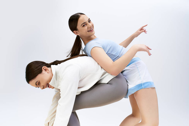 Zwei hübsche, brünette Teenager-Mädchen in sportlicher Kleidung zeigen in einem Studio vor grauem Hintergrund ihre Tanzschritte. - Foto, Bild