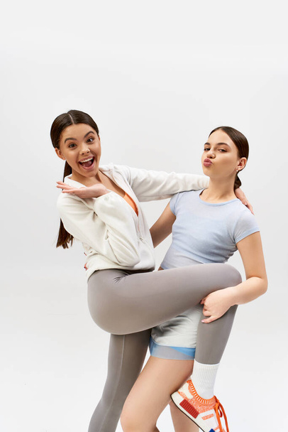 Two pretty, brunette teenage girls in sportive attire, posing in a studio against a grey background. - Photo, Image