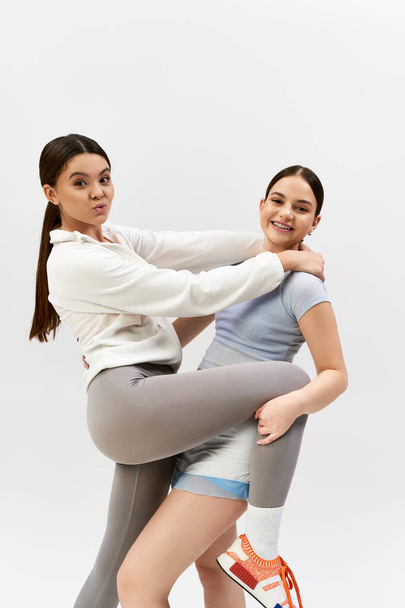 Zwei hübsche, sportliche Teenager-Mädchen in sportlicher Kleidung posieren gemeinsam in einem Studio vor grauem Hintergrund. - Foto, Bild