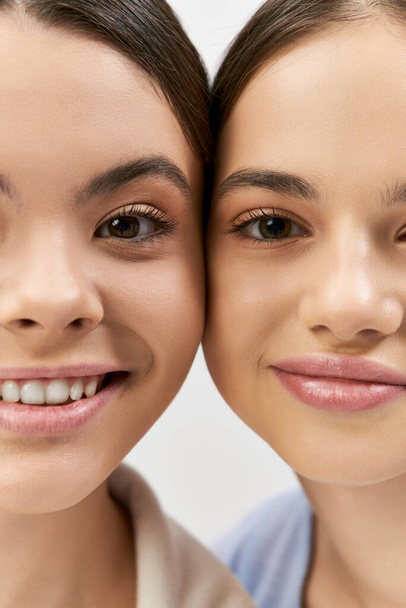 twee mooi en brunette tiener meisjes nemen een selfie in een studio tegen een grijze achtergrond. - Foto, afbeelding