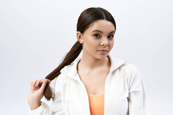 A brunette teenage girl with a ponytail wearing sportive attire against a grey studio backdrop. - Photo, Image