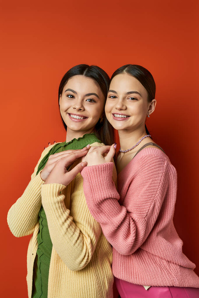 Dwie ładne i brunetka nastolatki w casual strój stojąc obok siebie przed śmiałą czerwoną ścianą w studio. - Zdjęcie, obraz