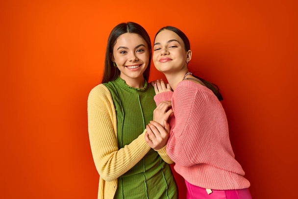 Zwei hübsche, lässige brünette Freundinnen stehen vor einer lebhaften orangefarbenen Wand und strahlen Vertrauen und Freundschaft aus. - Foto, Bild