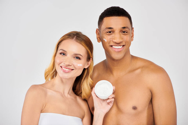 A trendy, diverse couple poses lovingly while applying facial cream. - Photo, Image