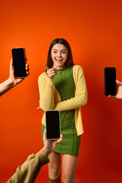 Молода дівчина в зеленій сукні впевнено стоїть біля багатьох мобільних телефонів - Фото, зображення
