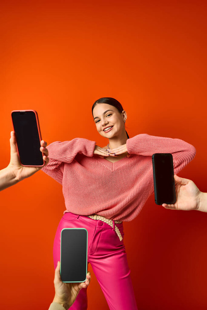 een brunette tiener meisje in roze in de buurt van mobiele telefoons tegen een oranje achtergrond in een studio. - Foto, afbeelding