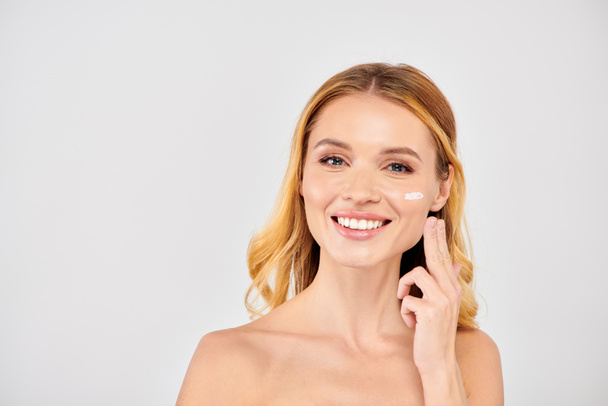 Jonge vrouw aanbrengen gezichtscrème tijdens huidverzorging routine. - Foto, afbeelding
