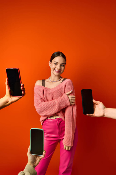A brunette woman stands before a red wall, near two cell phones in hands of people - Photo, Image