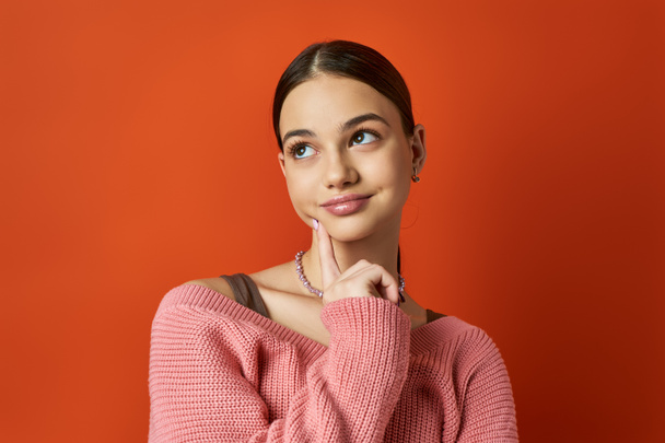 A brunette teenage girl in a pink sweater strikes a pose for a photo in a vibrant studio setting. - Photo, Image