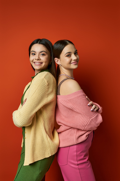 Дві красиві брюнетки дівчата-підлітки в повсякденному вбранні стоять поруч один з одним перед яскравою червоною стіною. - Фото, зображення