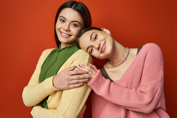 twee mooie brunette tiener meisjes, vrouwelijke vrienden, staan zij aan zij in casual kleding op een oranje studio achtergrond. - Foto, afbeelding