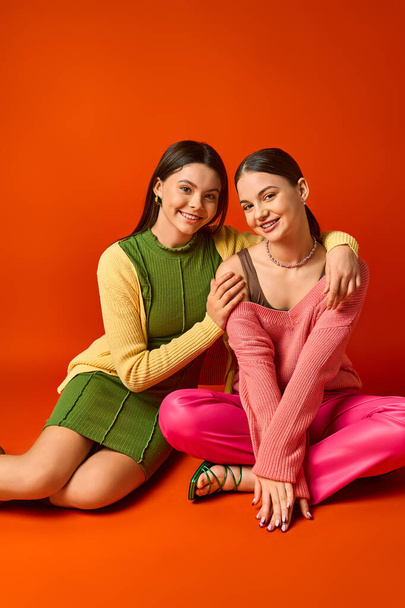 Deux adolescentes brunes en tenue décontractée posant joyeusement sur un fond orange dans un décor de studio. - Photo, image