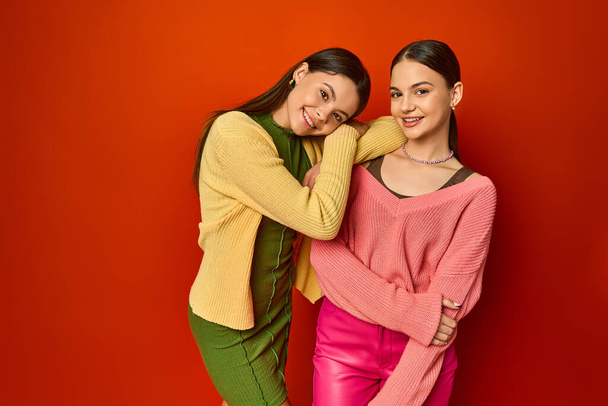 Zwei hübsche Brünetten, Teenager-Freunde, stehen zusammen vor einer leuchtend roten Wand in einem Studio-Setting. - Foto, Bild