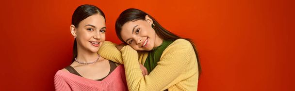 Két csinos, barna tinédzser lány áll egymás mellett egy élénk vörös fal előtt, barátsággal és magabiztossággal.. - Fotó, kép