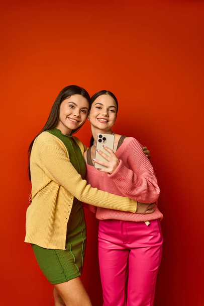 Dvě hezké dospívající dívky, brunetky a ležérně oblečené, stojící bok po boku před zářivou červenou zdí. - Fotografie, Obrázek