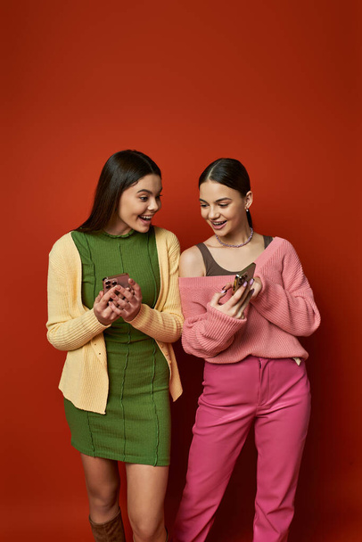 Dvě hezké, brunetky dospívající dívky stojí bok po boku, vyzařuje přátelství a kamarádství, na živém oranžovém pozadí. - Fotografie, Obrázek