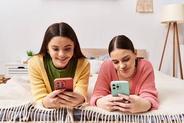 Due ragazze adolescenti in abbigliamento casual si rilassano su un letto, assorte nei loro telefoni cellulari. - Foto, immagini