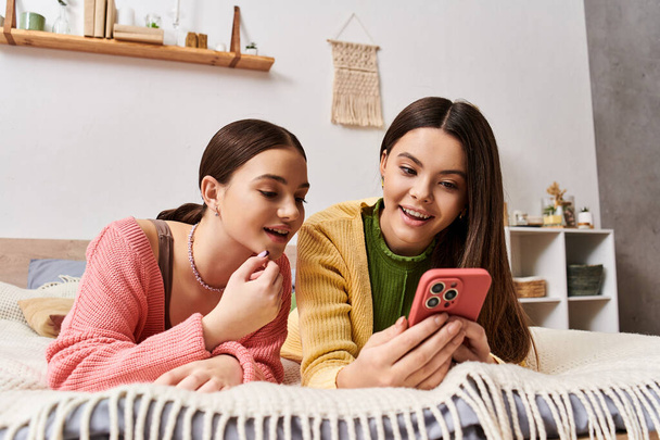 Twee vrouwen in casual kleding, op een bed, glimlachend, samen naar een mobiel scherm kijkend. - Foto, afbeelding