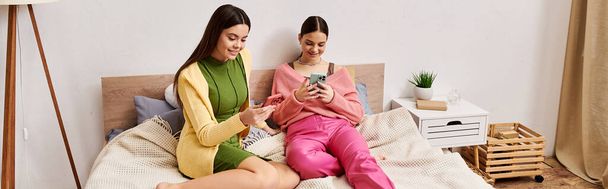 Duas jovens em traje casual sentadas em uma cama, absorvidas em um telefone celular. - Foto, Imagem