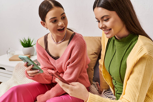 Due donne in abbigliamento casual si siedono su un divano, impegnate in una conversazione mentre guardano un telefono cellulare. - Foto, immagini