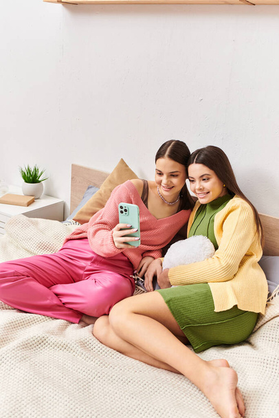 Due donne, belle amiche adolescenti, sedute su un letto e assorte in uno schermo del cellulare. - Foto, immagini