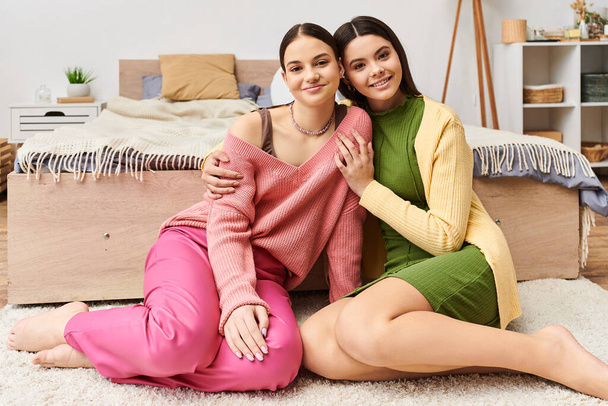 Twee stijlvolle jonge vrouwen in casual kleding zitten op de vloer poseren samen voor een modieuze shot. - Foto, afbeelding