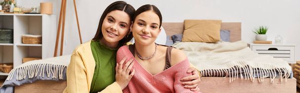 Due belle ragazze adolescenti in abbigliamento casual chattano e ridono mentre si siedono uno accanto all'altro su un letto a casa. - Foto, immagini