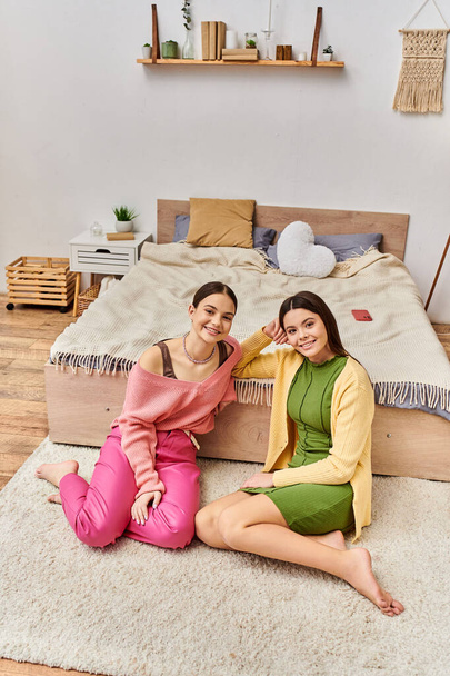 Две симпатичные девочки-подростки в повседневной одежде сидят на полу перед кроватью, общаются и отдыхают вместе дома. - Фото, изображение
