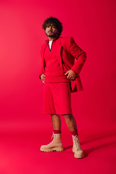 Guapo joven indio posando en una chaqueta roja y pantalones cortos sobre un fondo rojo vivo. - Foto, imagen