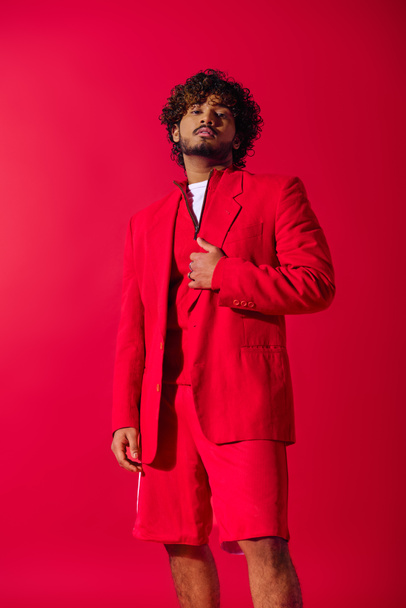 Stylish young Indian man in red suit strikes a pose against a vibrant backdrop. - Photo, Image