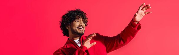 Un joven indio guapo con una chaqueta roja vibrante golpea un gesto dramático. - Foto, imagen
