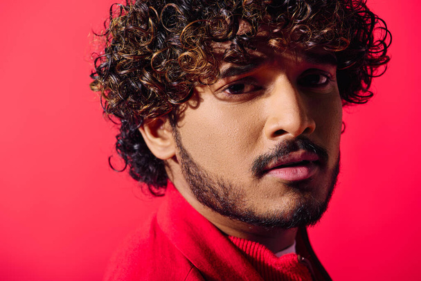 A close-up of a handsome young Indian man with curly hair and intense gaze, posing against a vivid backdrop. - Photo, Image