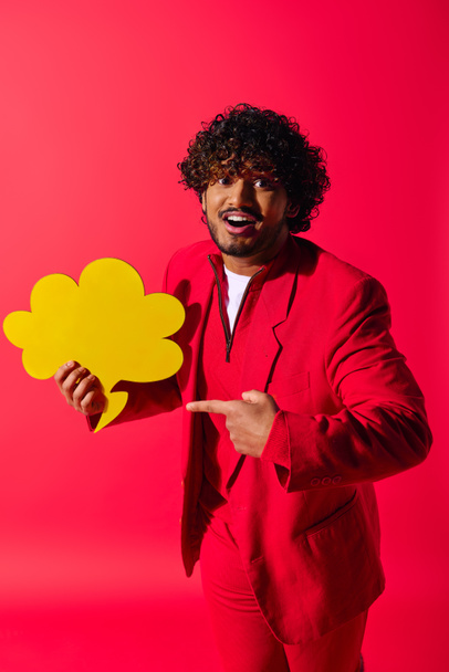 Kırmızı takım elbiseli yakışıklı genç adam canlı bir arkaplanda sarı bir konuşma balonu tutuyor.. - Fotoğraf, Görsel