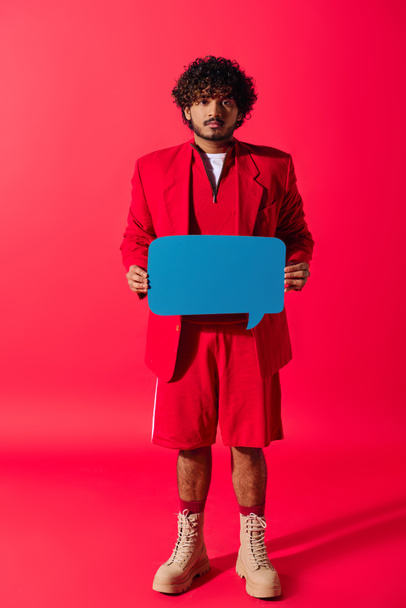 Lebendiger junger Mann im roten Anzug hält blaue Sprechblase. - Foto, Bild