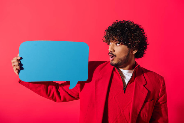 Handsome man in red jacket confidently presents blue speech bubble. - Photo, Image