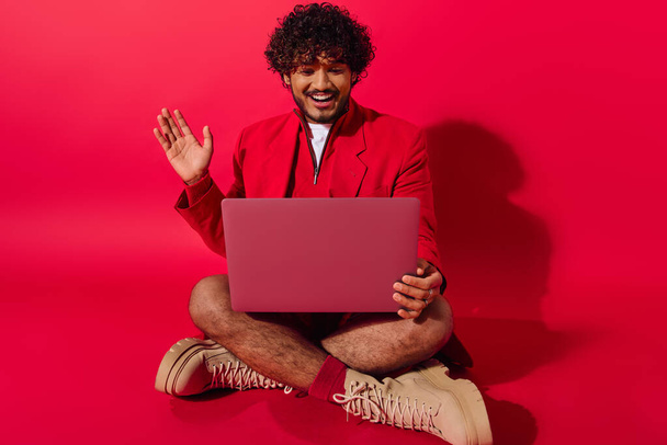 Mężczyzna w żywym ubraniu, siedzący na podłodze, pochłonięty pracą na laptopie.. - Zdjęcie, obraz
