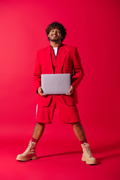 Όμορφος νεαρός Ινδός με κόκκινη στολή ποζάρει με φορητό υπολογιστή. - Φωτογραφία, εικόνα