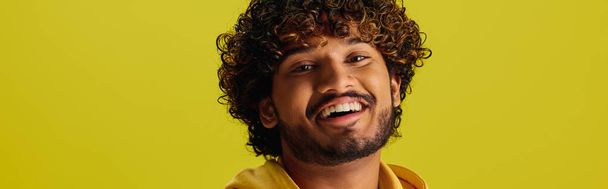 Un guapo joven indio con el pelo rizado posando en una vibrante camisa amarilla. - Foto, imagen