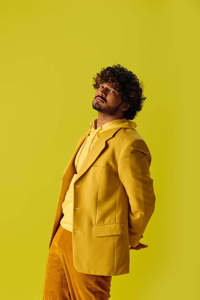 Knappe jonge Indiase man in levendige outfit poseert voor een heldere gele muur. - Foto, afbeelding