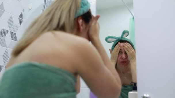 Een vrouw staat voor een badkamerspiegel en kijkt naar haar spiegelbeeld. Ze lijkt haar haar aan te passen en haar uiterlijk te controleren.. - Video