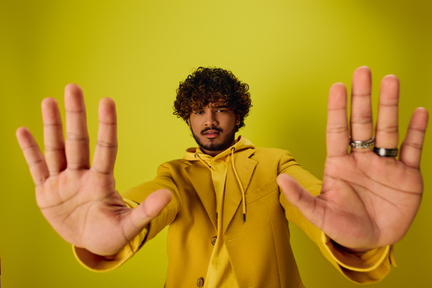 A handsome young Indian man in a yellow hoodie is holding out his hands. - Photo, Image