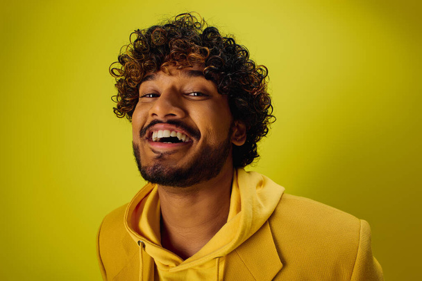 Hombre indio guapo con el pelo rizado posa con confianza en una sudadera con capucha de color amarillo brillante. - Foto, imagen
