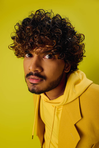Bello giovane indiano con i capelli ricci posa in una camicia gialla vibrante. - Foto, immagini