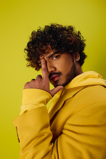Handsome Indian man in yellow hoodie striking a pose on a vibrant backdrop. - Photo, Image