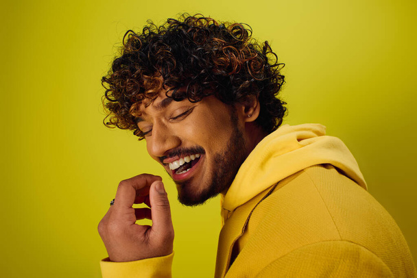 A handsome young Indian man with curly hair striking a pose in a vibrant yellow jacket on a vivid backdrop. - Photo, Image