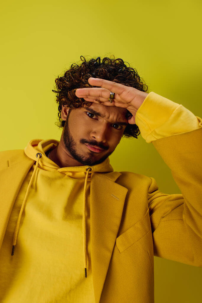 Guapo joven indio con el pelo rizado posando en una vibrante sudadera con capucha amarilla. - Foto, Imagen