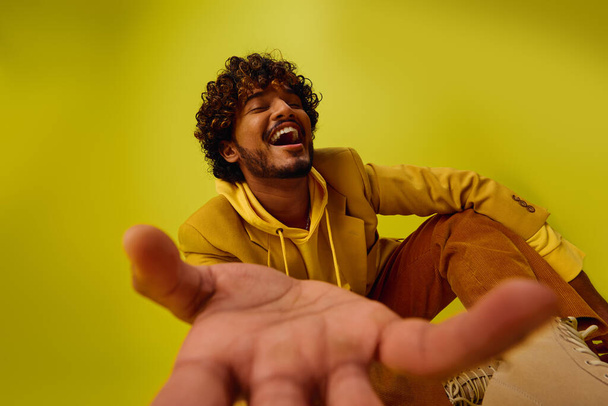 Ένας όμορφος νεαρός Ινδιάνος ποζάρει με μια κίτρινη κουκούλα, απλώνοντας το χέρι του προς τα έξω.. - Φωτογραφία, εικόνα